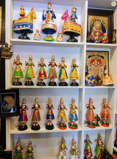 Colorful Thanjavur dolls alongside framed Thanjavur paintings for sale in Tamil Nadu