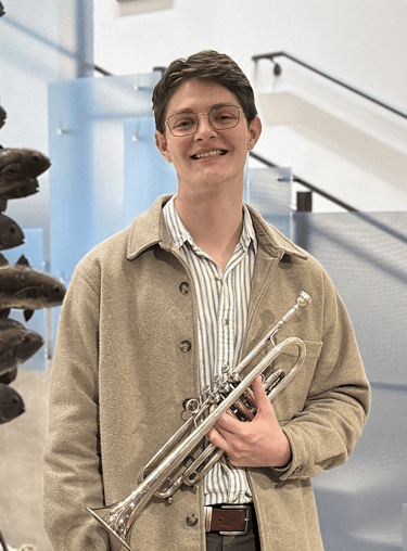 Jacob West in a jacket and glasses holding a trumpet