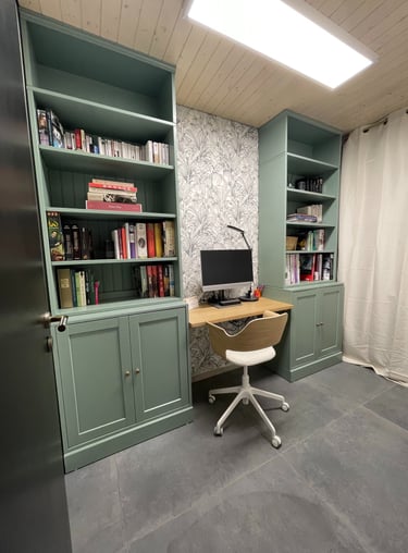 Home office with sage green built-in bookshelves, a wooden desk, and floral wallpaper.