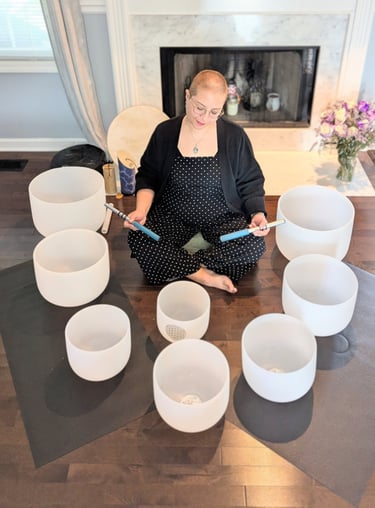 Cricia sits in the floor surrounded by white crystal singing bowls for a sound healing session.