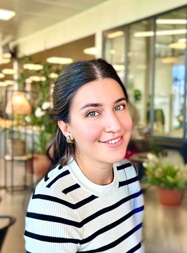 Smiling brunette woman wearing a striped sweater in a bright modern office setting.