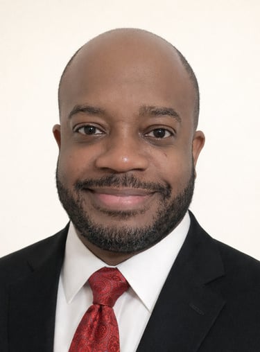 Professional headshot of a smiling Black businessman wearing a black suit and red patterned tie.