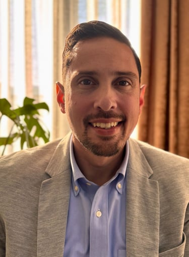 A smiling professional man in a grey blazer and blue shirt posing for a business headshot.