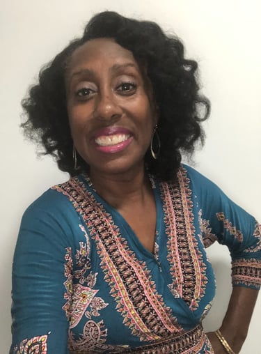 Smiling African American woman with curly hair wearing a teal patterned blouse.