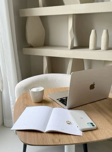 Minimalist home office setup with a laptop, open notebook, coffee cup, and shelves in the background