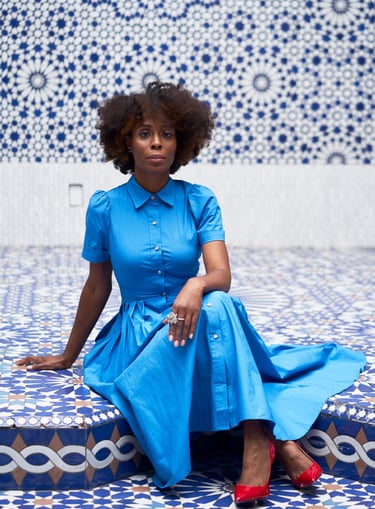 Founder of Emisha Wellness in a blue dress, red shoes in a blue & white MOR tile foyer