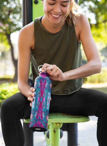a woman sitting on a bench in a park with a water bottle that has an abstract pattern