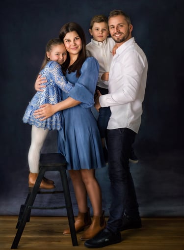 a family of four posing in a studio for a family portrait, all wearing blue and white