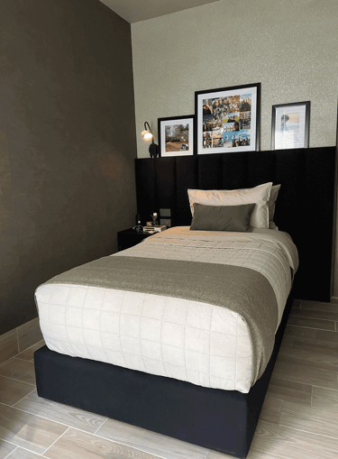 Recámara con cama individual, cojines neutros y galería de fotos sobre cabecera | KARÄNA