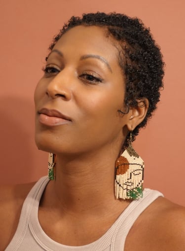 A woman with a white tank top wearing a pair of  earrings beaded by hand with a face pattern