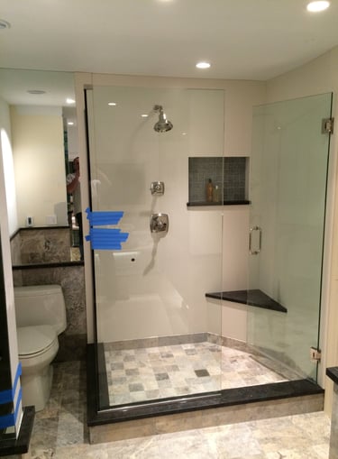 Modern walk-in shower with frameless glass doors, marble tile floor, and a built-in corner bench seat.