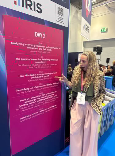 a woman standing in front of a sign that says Elysian Services HR Ltd speaker slot at Accountex