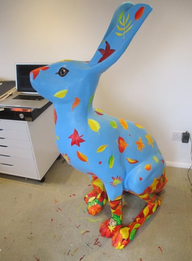 A hare sculpture with autumn leaves and wildlife painted by Laura Fearn
