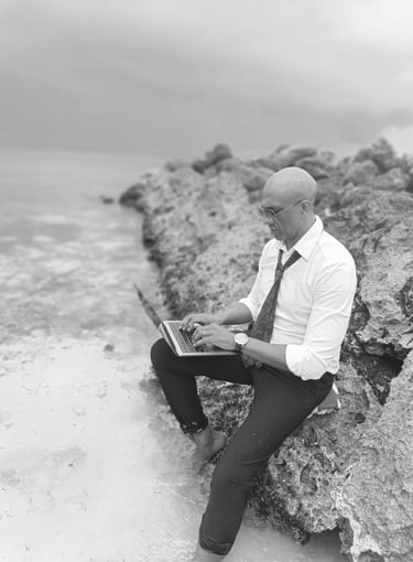 « Bruno Valery travaillant sur son ordinateur, assis sur un rocher les pieds dans l’eau en Guadeloupe »