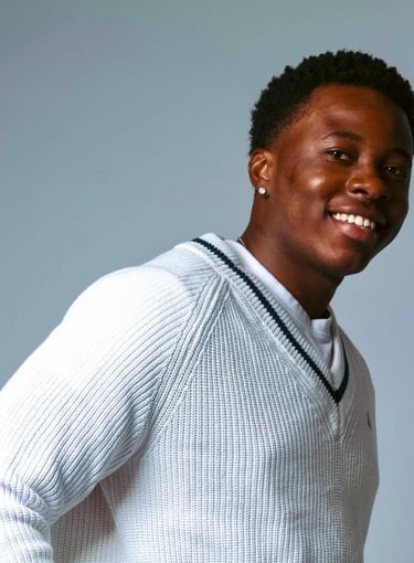 a man in a white sweater and jeans standing in front of a gray background