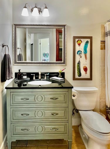 Bathroom with vintage emerald vanity, black granite countertop, and beveled glass mirror.