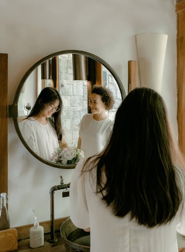 a woman in a white shirt is looking at her reflection in a mirror
