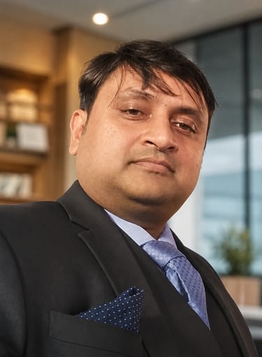 Professional portrait of a businessman wearing a black suit and blue tie in a corporate office setting.
