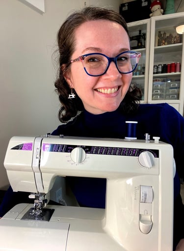 Close-up of a woman with glasses and brown hair smiling behind a sewing machine.