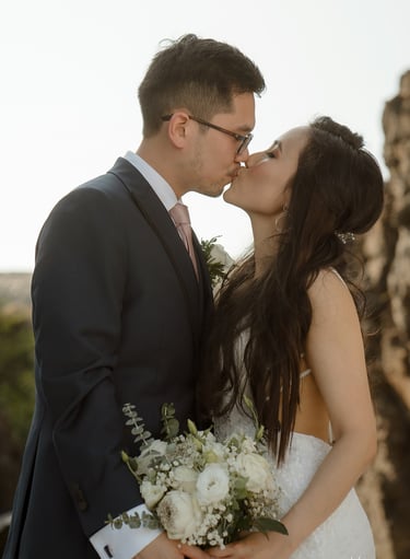a bride and groom kissing in front of a cliff