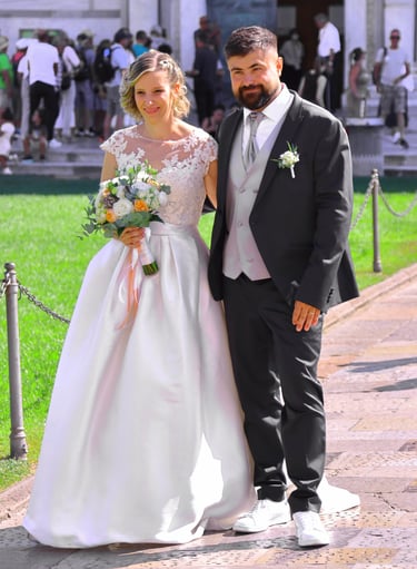 Bride and groom posing together outside a historic cathedral during their wedding ceremony on a sunny day.