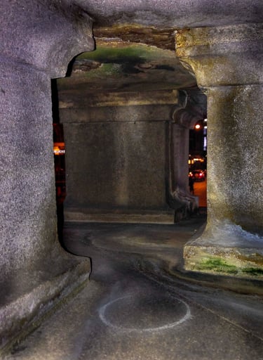 Inside of the stone sculpture base with pillars and glimpses into a street life at night.