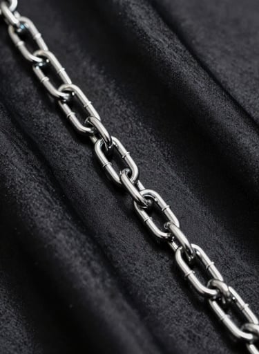 A macro photography shot of a thick chrome chain lying across deep black satin fabric, with sharp highlights and edgy shadows, modern minimalist style.
