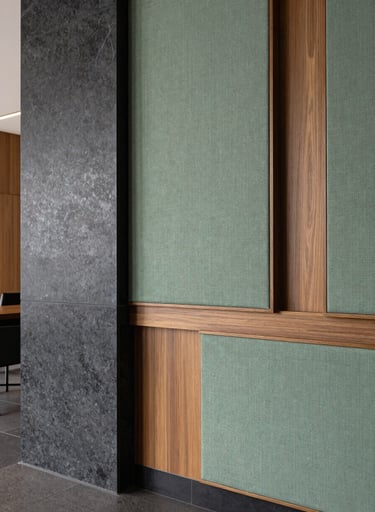 Detailed shot of interior textures in a South American office lobby: sage green textile panels next to polished charcoal stone and warm taupe wood accents. Elegant and professional photography style.