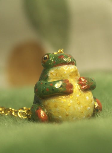 Close-up of a small polymer clay green and gold frog pendant necklace on soft fabric background
