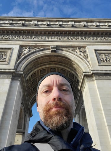 a man with a beard and a beard in front of a arc de trios