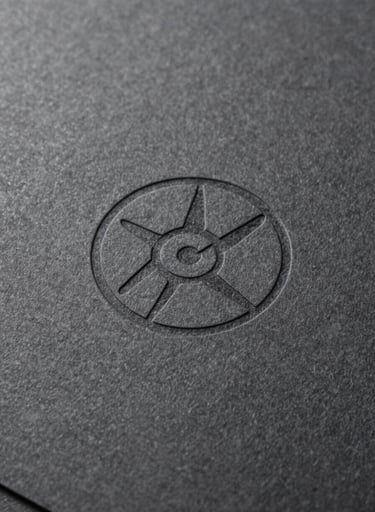 A desaturated, close-up photograph showing the texture of high-quality charcoal-colored paper with a subtle embossed logo. Soft natural light highlights the grain and craft, reflecting a premium art direction approach.