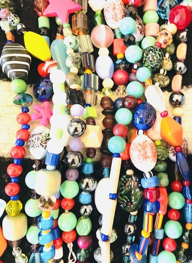 A colorful collection of handmade necklaces featuring vibrant glass beads, stars, and diverse textures.