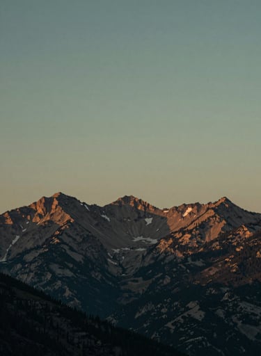A stunning, atmospheric outdoor photography shot of a North American / US mountain range at dusk. The sky is a muted charcoal and sage green, conveying a thought-provoking and calm mood. High-resolution cinematic quality.