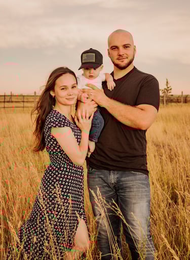 a man and woman standing in a field holding a baby
