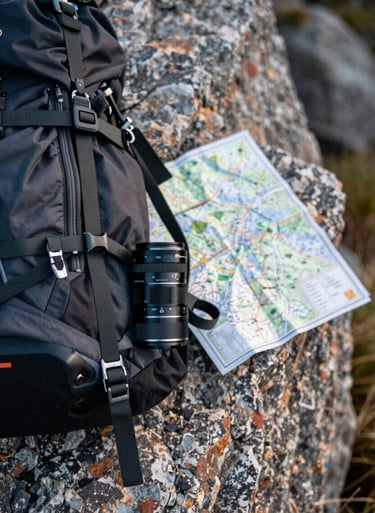 Close-up of adventure gear and a map on a rocky ledge. The aesthetic is rugged yet elegant, focused on real-world storytelling.