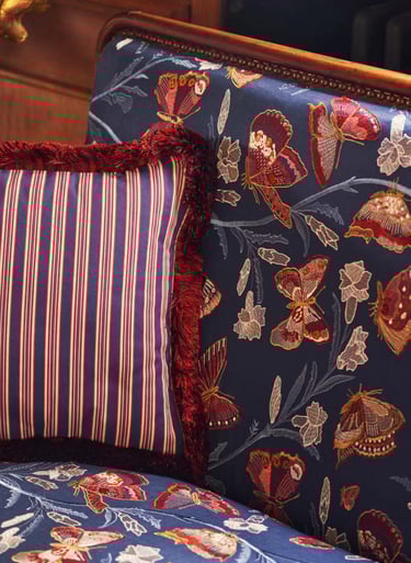 Banquette couverte d'un tissu bleu aux papillons et un coussin à rayures et marabout rasé