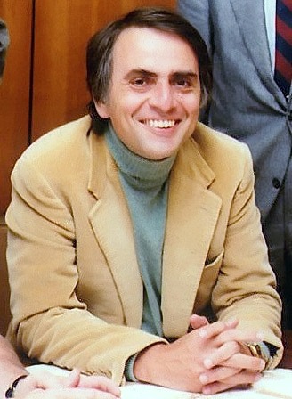 Carl Sagan in a suit and tie smiling at the camera