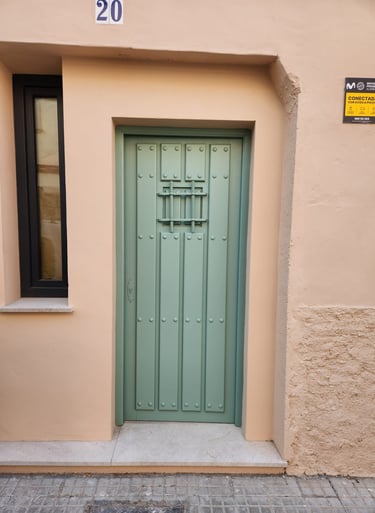 Rustic sage green wooden door with iron grilles on a beige Mediterranean building facade.