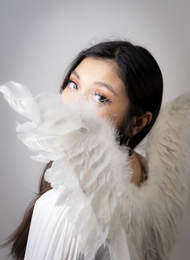 A self portrait, mostly white, over the shoulder peeking at camera through angel wings.
