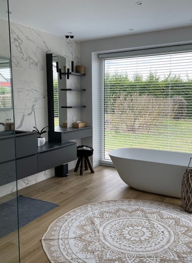 Modern bathroom with marble walls, double vanity, and a freestanding oval bathtub by a large window.