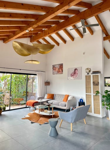 Modern living room with exposed wood ceiling beams, a grey sectional sofa, and gold leaf pendant lights.