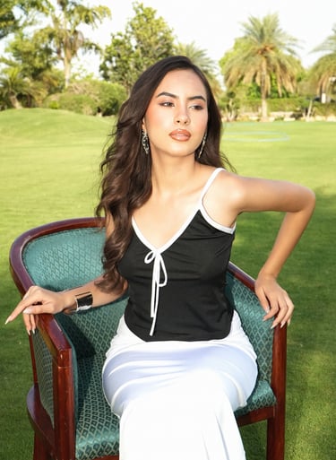 A stylish woman in a black and white top posing on a green chair in an outdoor garden setting.