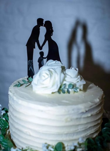 White tiered wedding cake with white roses and a silhouette cake topper of a bride, groom, and child.