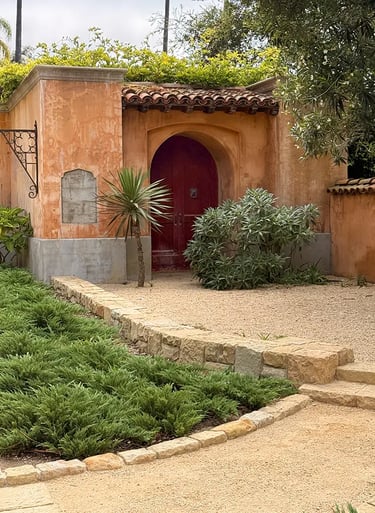 Weathered orange stucco wall with arched gate leading to Montecito, California estate.
