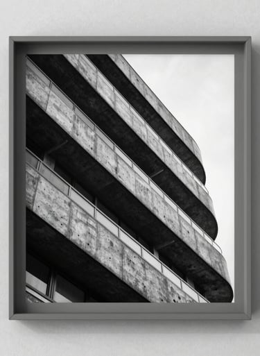 A black and white architectural photograph in a simple warm grey frame, hanging on a textured wall, clean and professional lighting.