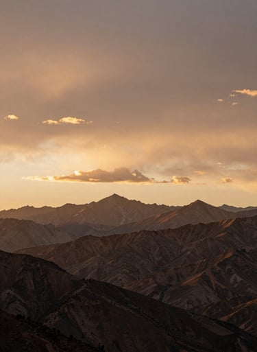 Wide cinematic sunset over a North American / US mountain range, warm earth brown and soft sand colored clouds.