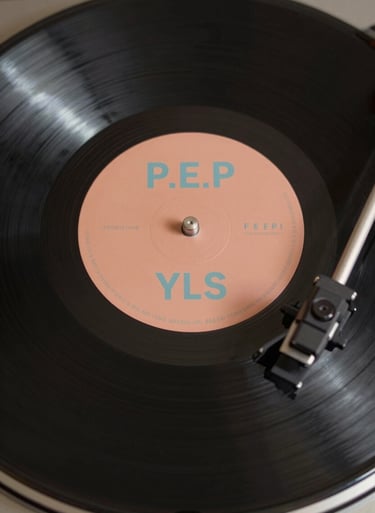 An overhead shot of a premium vinyl record spinning, the label featuring P.E.P YLS branding in #F5F5EB on a #3D2C20 background, warm and inviting atmosphere.