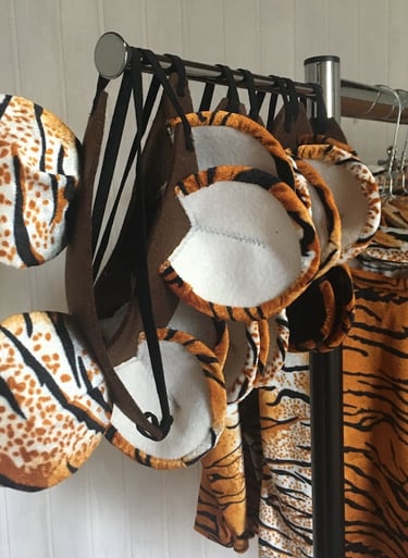 Handmade tiger ear headbands and matching animal print costumes hanging on a clothing rack.