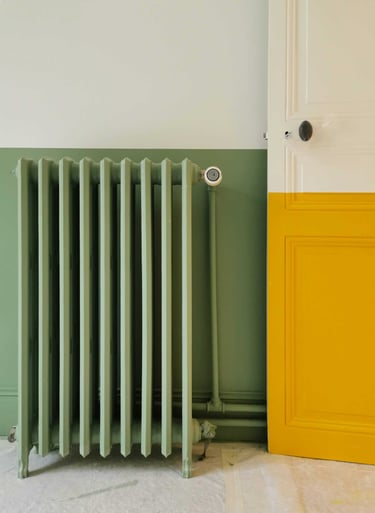 Vintage sage green radiator next to a yellow and white paneled door in a modern room.
