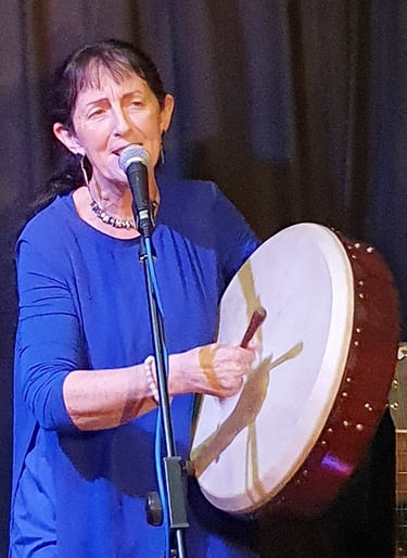 paula ryan in a blue dress is holding a drum and a microphone